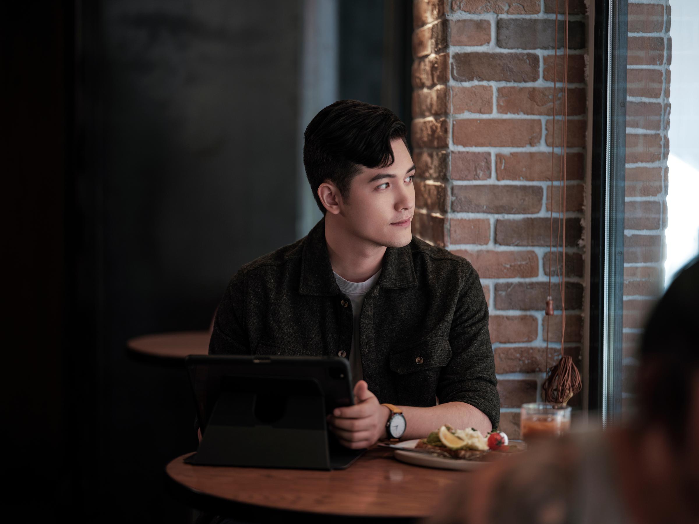 A man in a bar or restaurant looking outside the window and holding an iPad