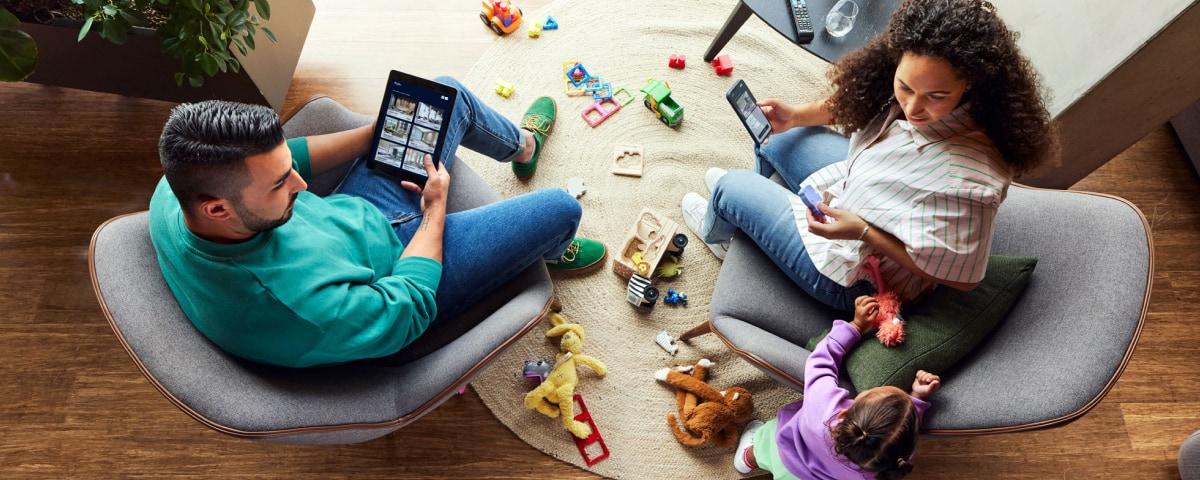 Top view of a family at home with parents using digital tablets and a toddler playing.