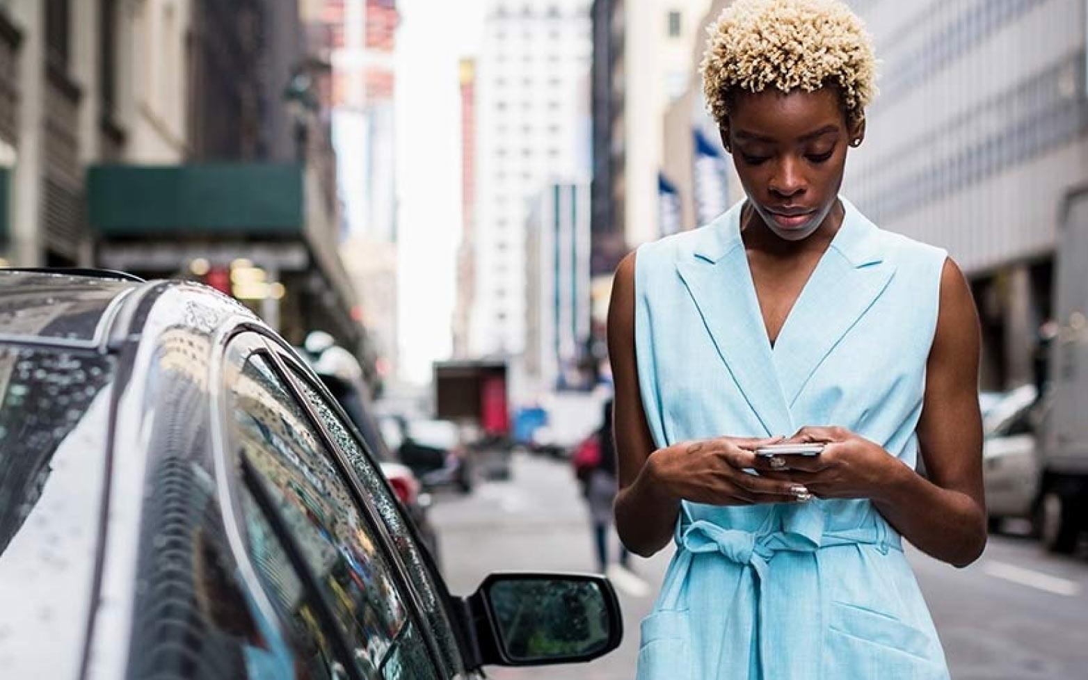 Kobieta w niebieskiej sukience używająca smartfona na ulicy
