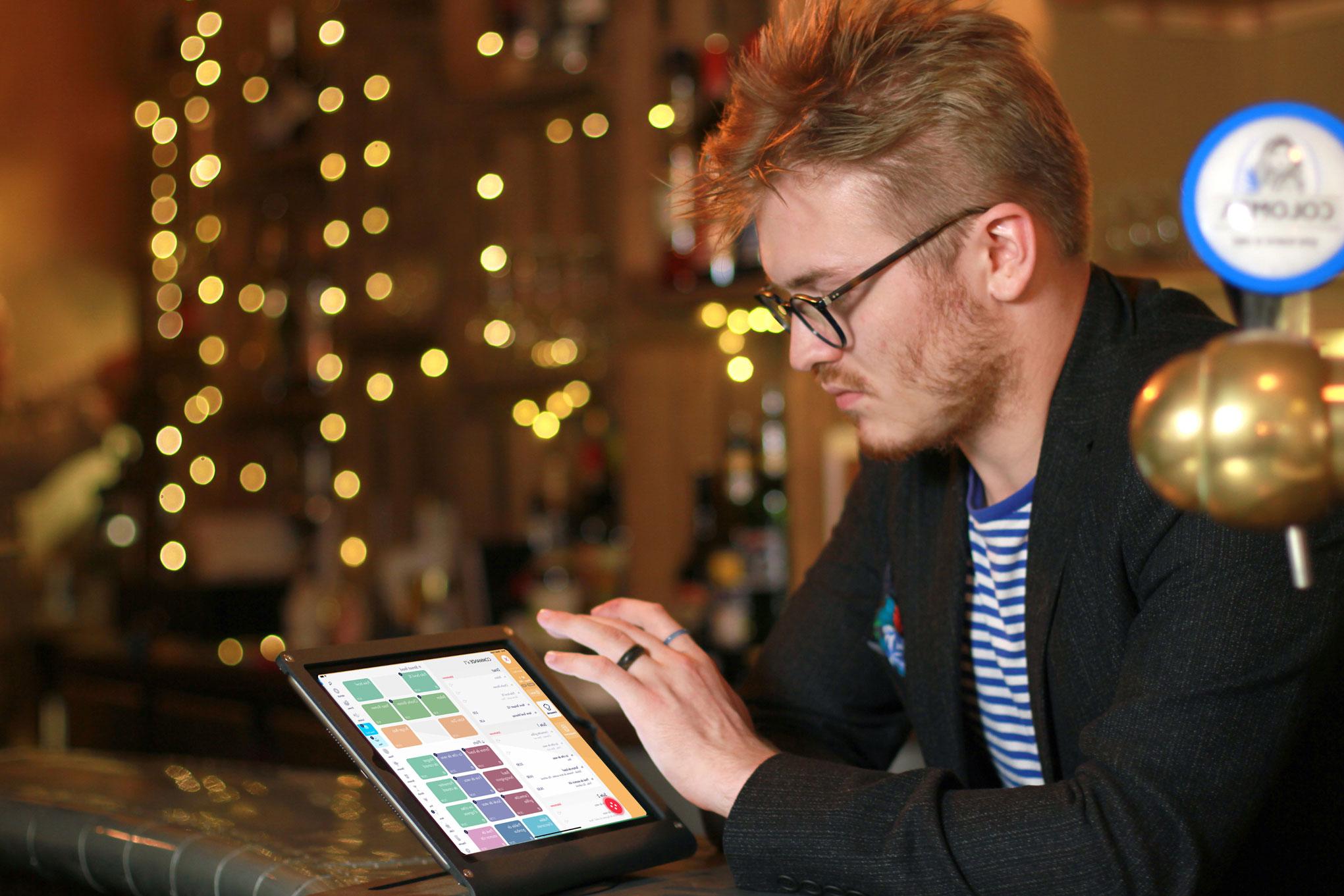 Homme interagissant avec un système de point de vente Adyen sur une tablette dans un cadre de café festif.