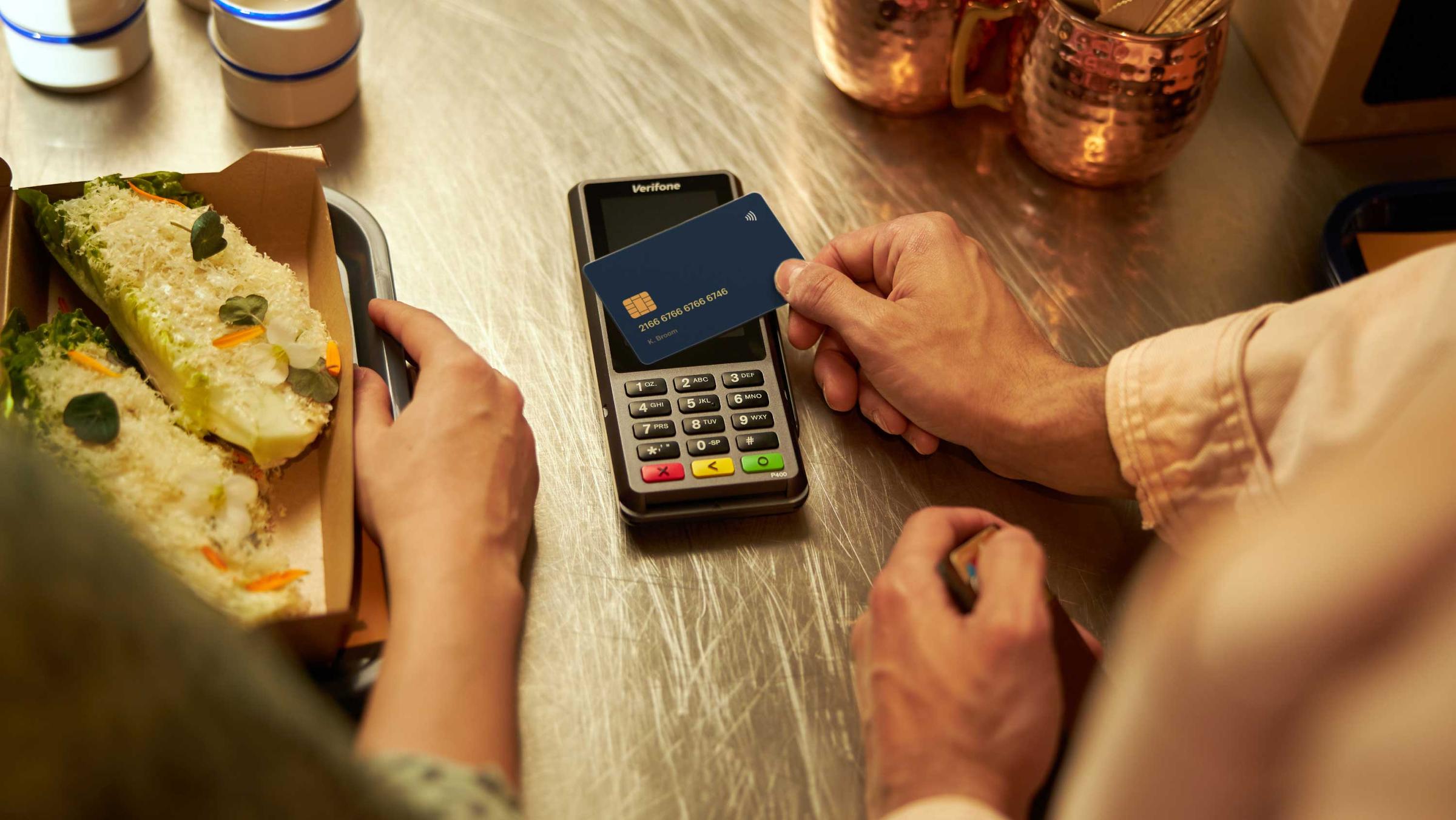 Person making a contactless payment with a credit card on a payment terminal at a cafe.