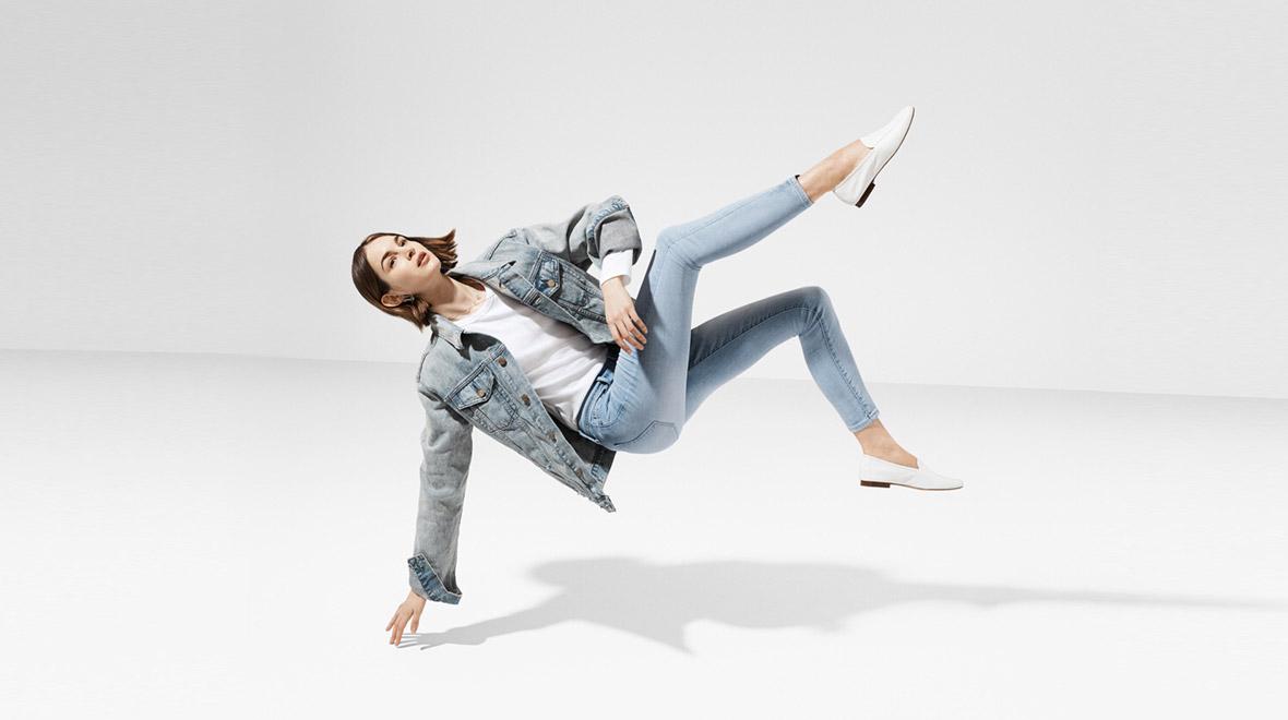 Mulher de jaqueta jeans azul e calças flutuando em um espaço branco vazio.