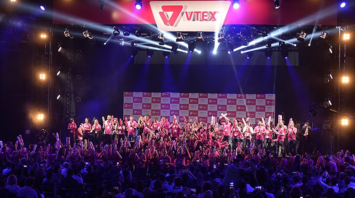 Palco com pessoas celebrando sob o logo VTEX em um evento