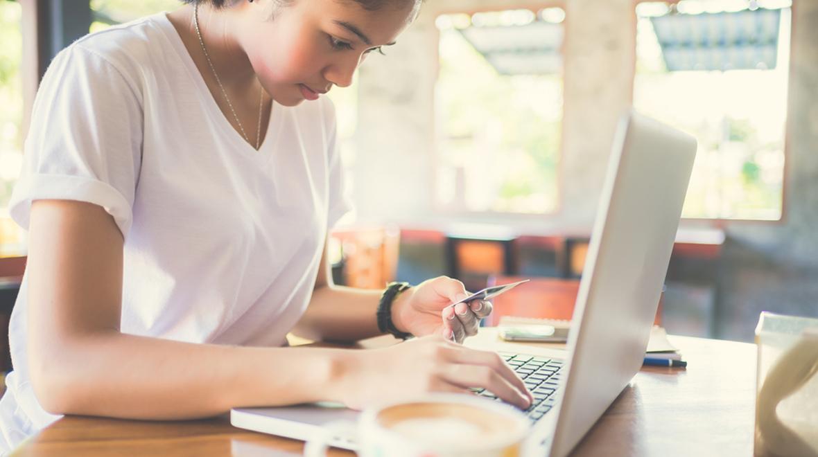Mulher usando laptop e segurando um cartão de crédito em um café
