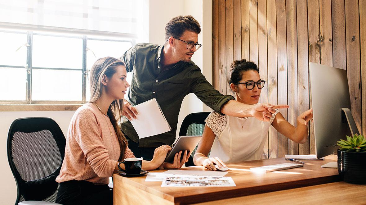 Três profissionais discutindo trabalho na mesa do computador.