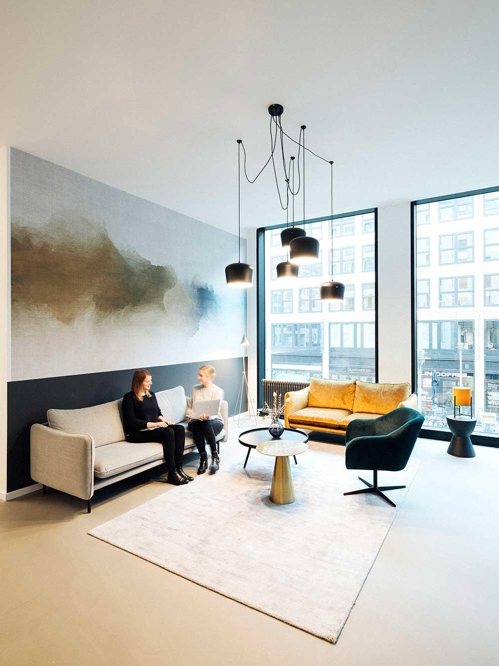 Two individuals conversing on a sofa in a modern lounge area with stylish decor.