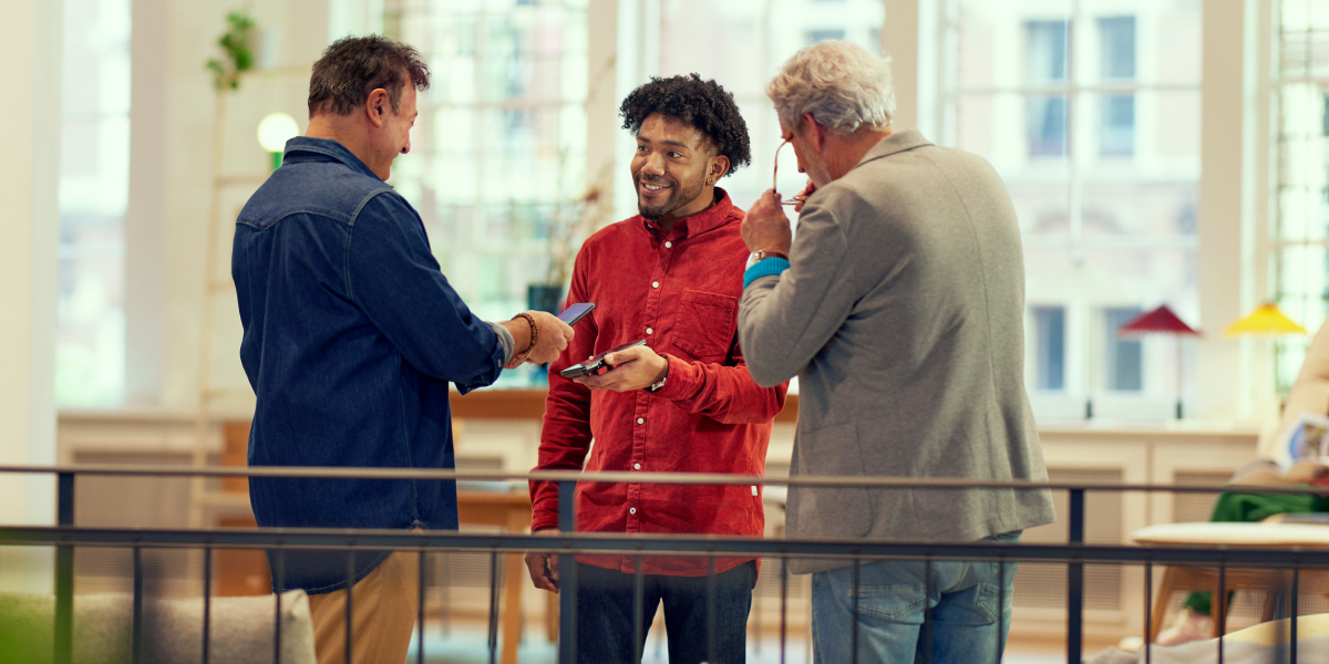 Tre personer som genomför en mobil betalningstransaktion i en ljus inomhusmiljö.