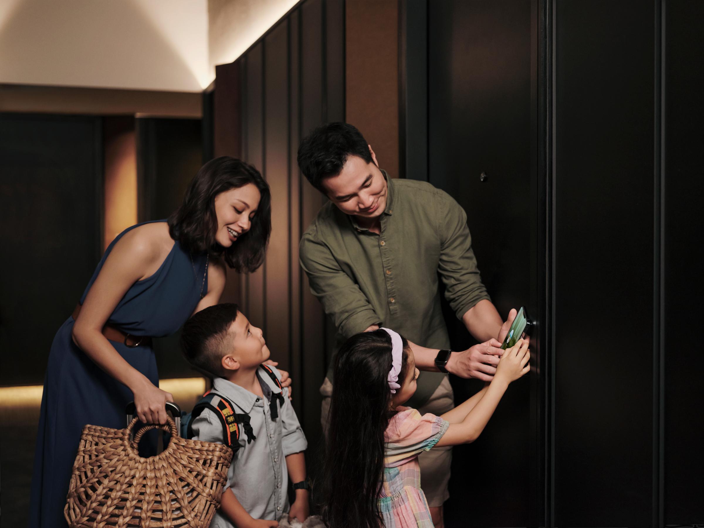 A family with children in a hotel corridor, opening their room with a card, after checking in at the hotel reception.