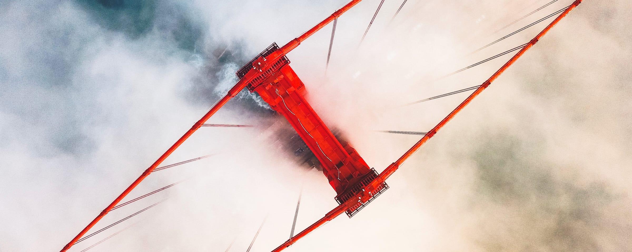 Aerial view of a red suspension bridge enveloped in mist.