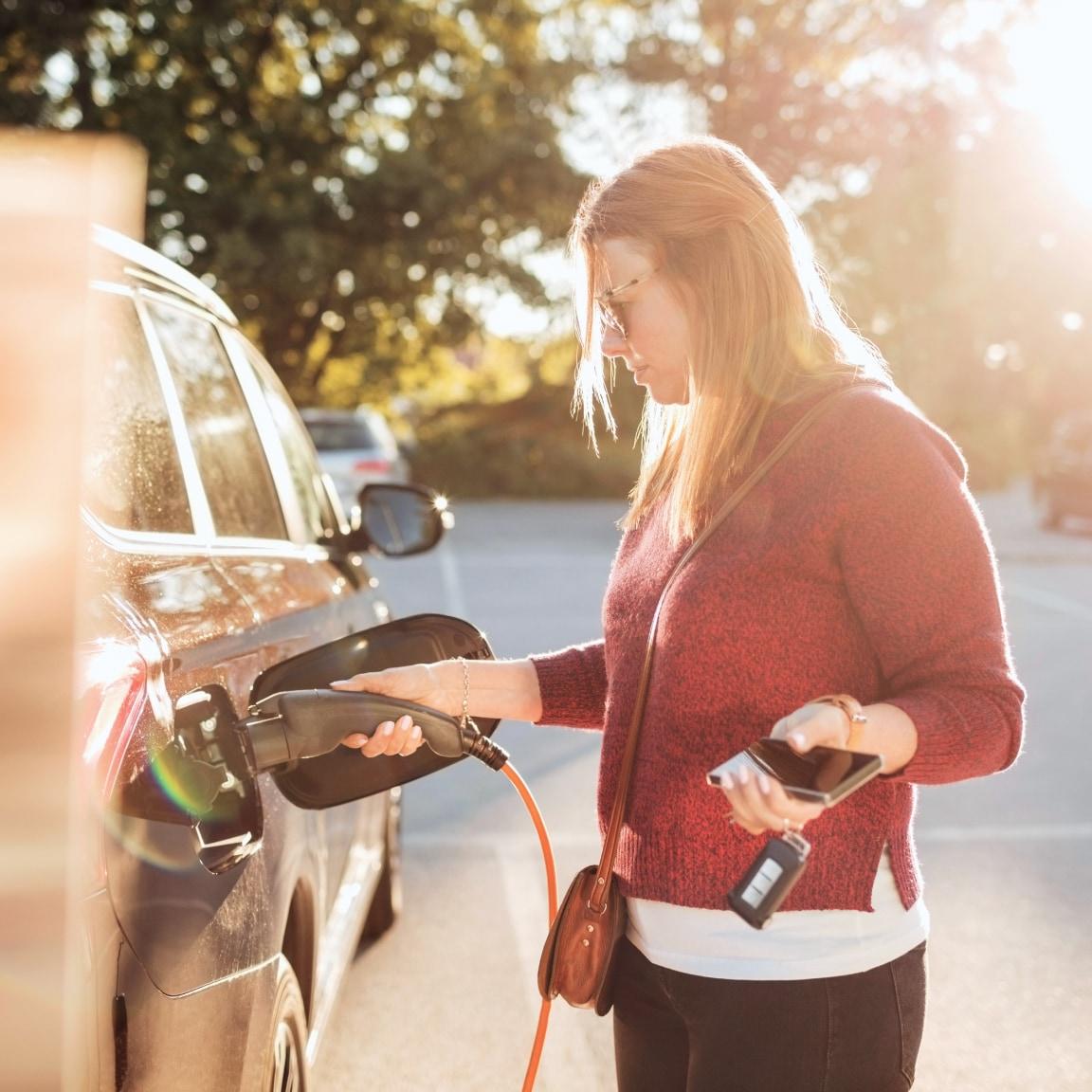 Kvinna använder en smartphone medan hon laddar en elbil.