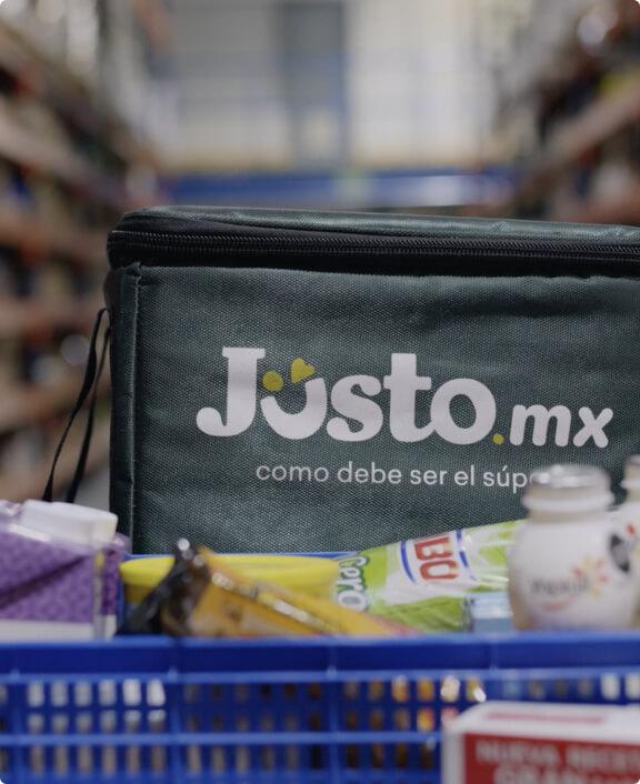 Primer plano de una cesta de compras con una bolsa de entrega Justo.mx llena de comestibles.