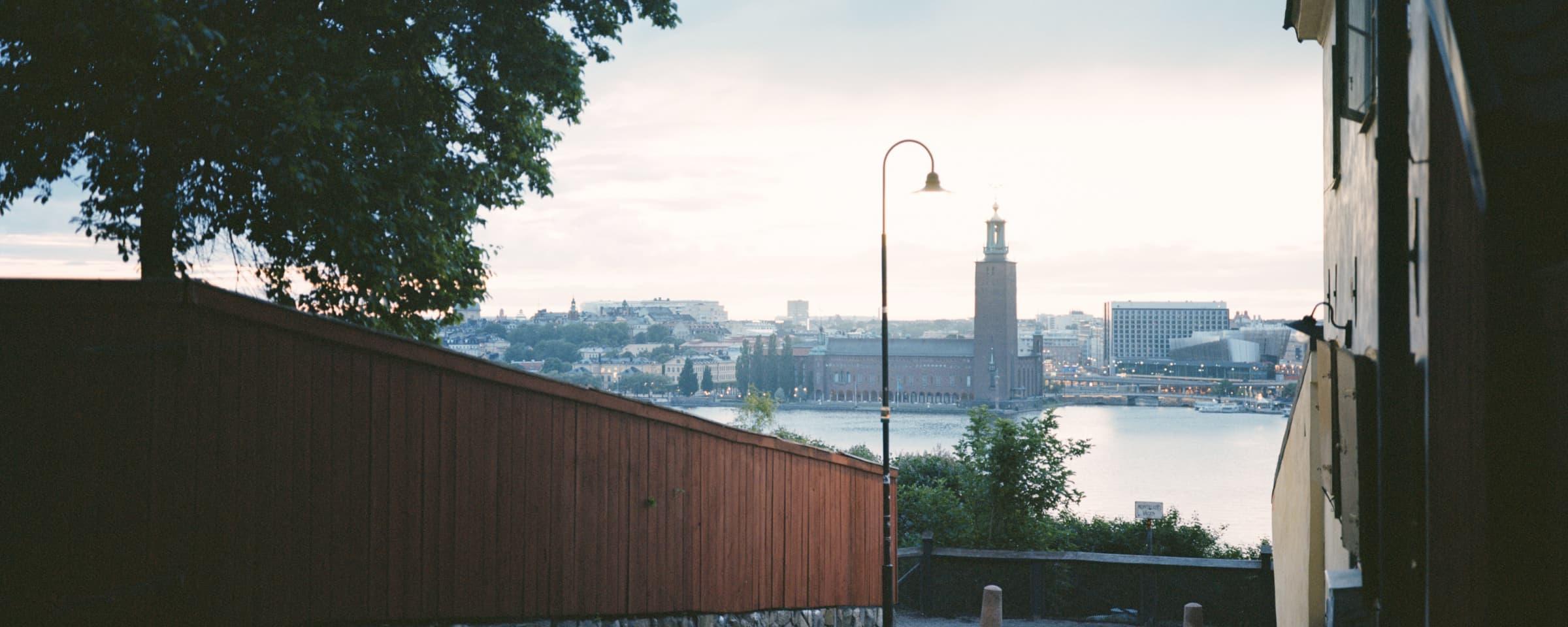 Skymningvy över en stadsbild med en framträdande torn nära vatten, sedd från en skuggig gränd.