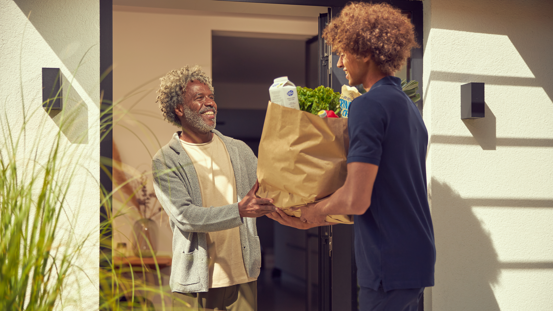 Smiling older man receiving a grocery delivery from a younger person at home.