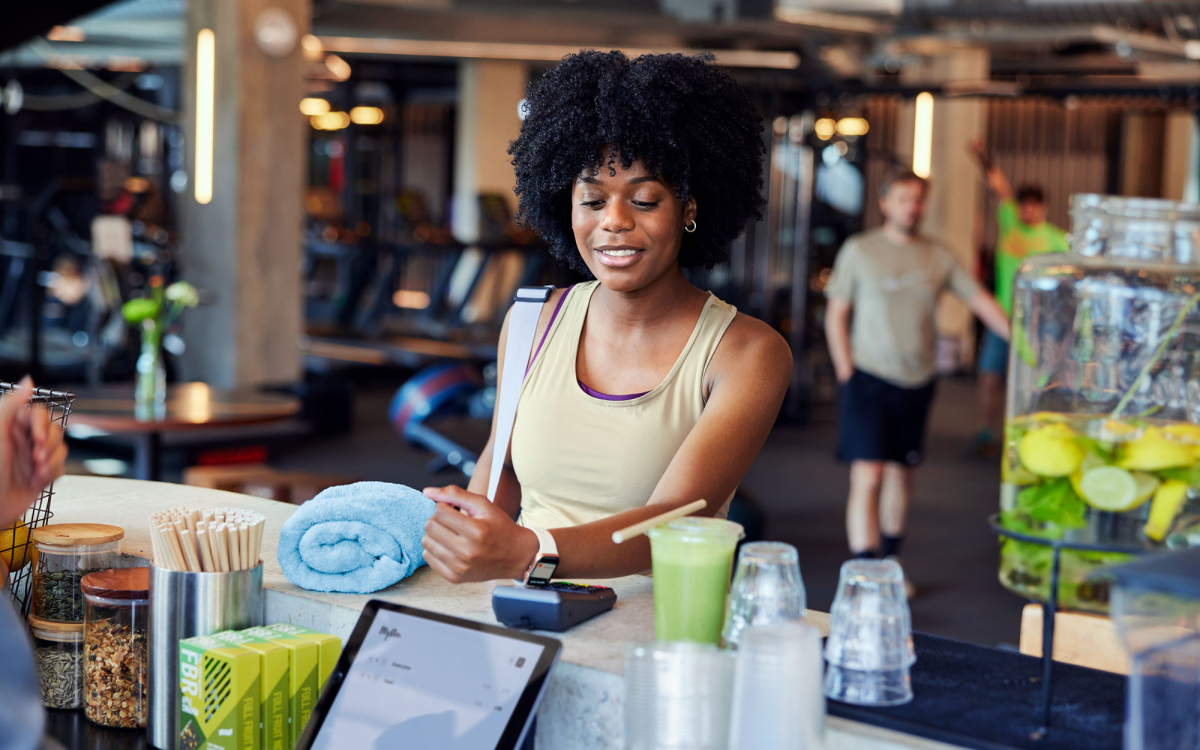 Donna in una palestra al bancone del juice bar che paga con una carta su un terminale di pagamento Adyen
