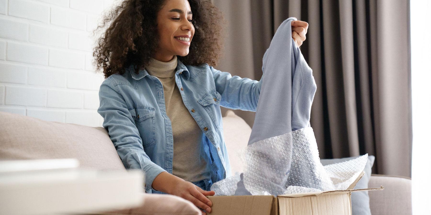 Smiling woman unpacking a cardboard box on a couch.
