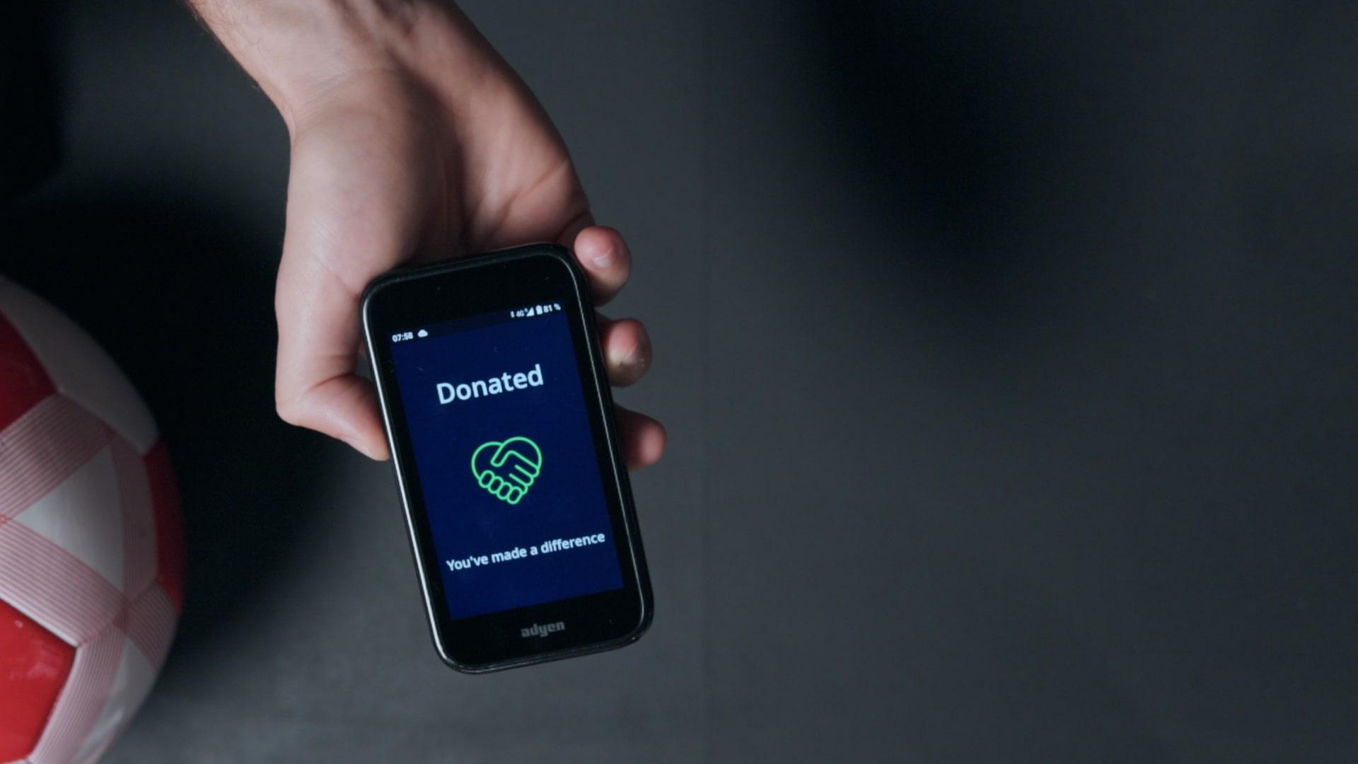 Hand holding smartphone displaying a donation confirmation screen with Adyen logo.