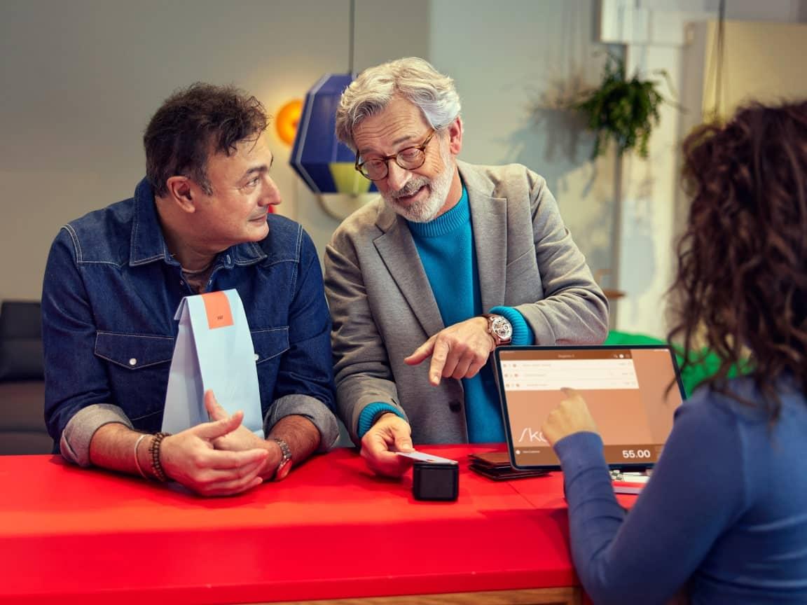 Two men discussing a transaction with a cashier using a digital payment terminal on a tablet.