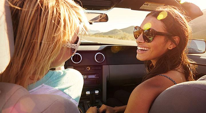 Deux femmes souriant l'une à l'autre assises dans une voiture avec un effet de flare solaire.
