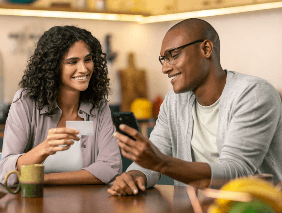 Duas pessoas sorrindo e olhando para um smartphone em um café