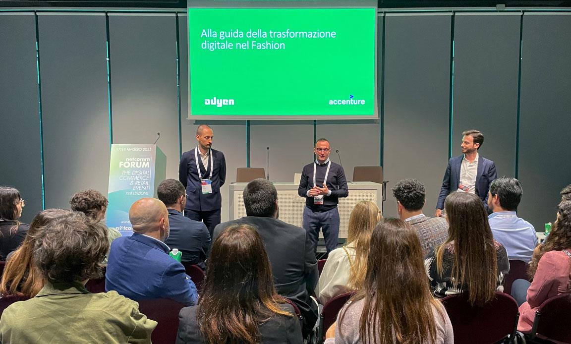 Relatori a una conferenza con pubblico e uno schermo che visualizza testo sulla trasformazione digitale nella moda, con Adyen e Accenture.