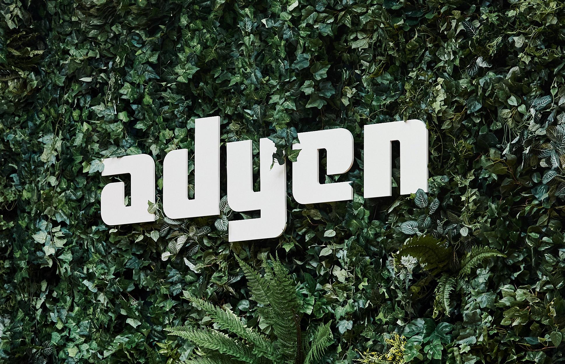 Adyen logo composed of white letters set against a dense green leafy background.