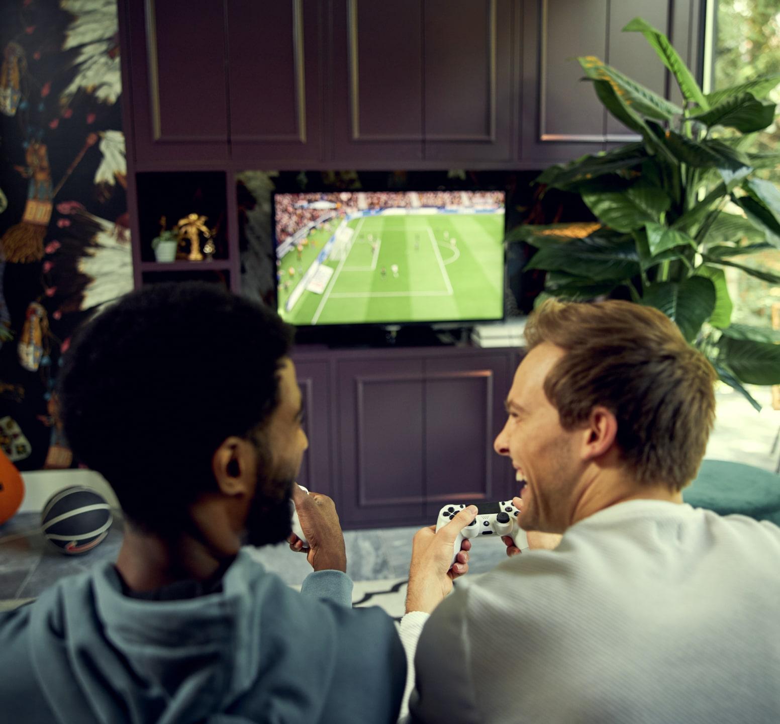 Dos personas jugando un videojuego de fútbol en una TV en una sala de estar acogedora.