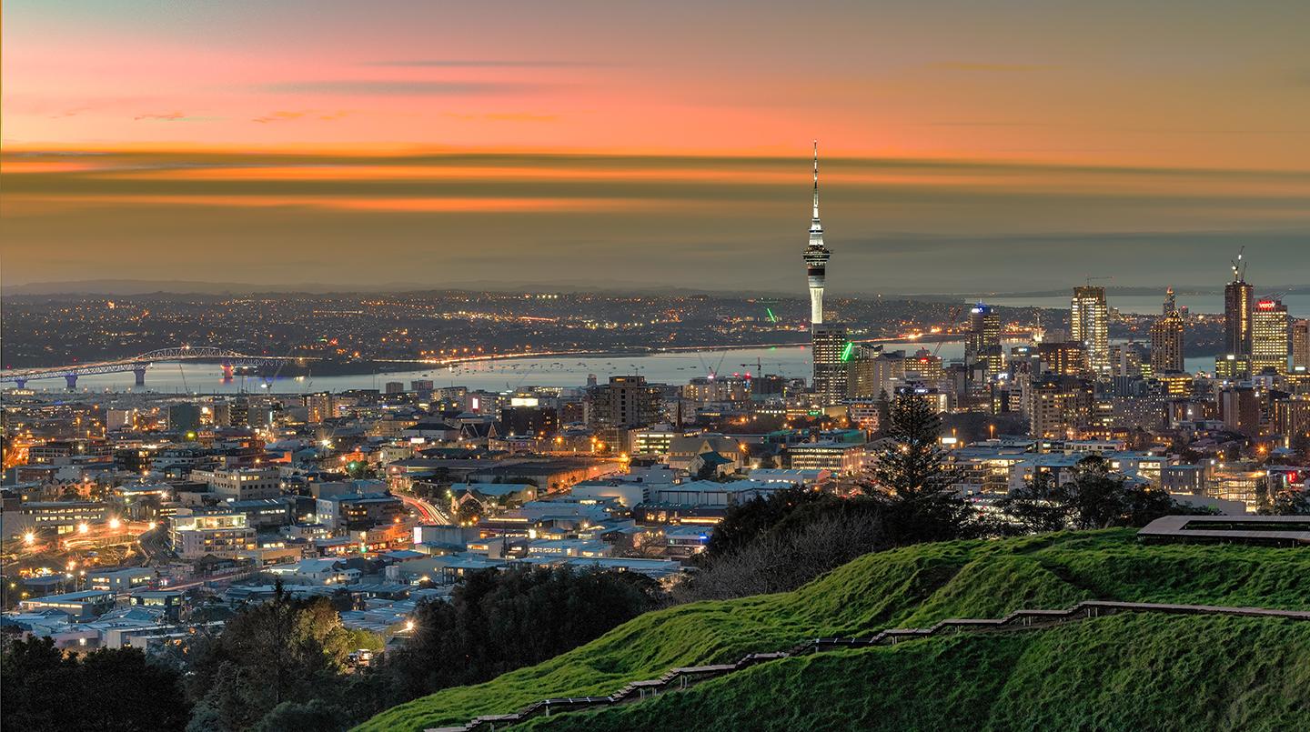 Twilight cityscape with lit buildings and a prominent tower under a gradient sky.