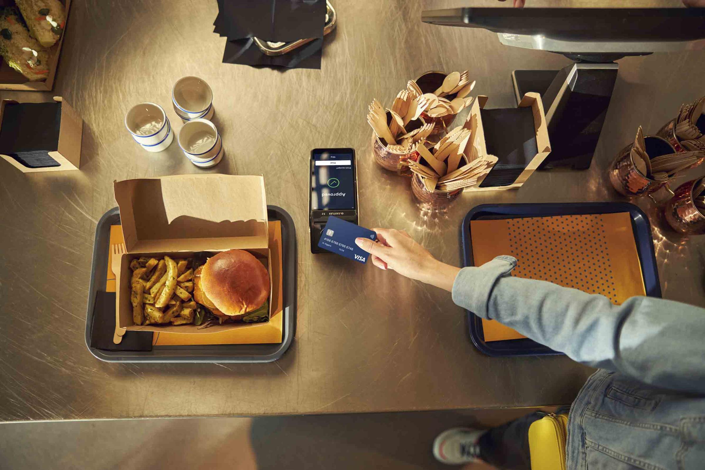 Person using a smartphone to make a contactless payment with an Adyen terminal at a fast-food restaurant.