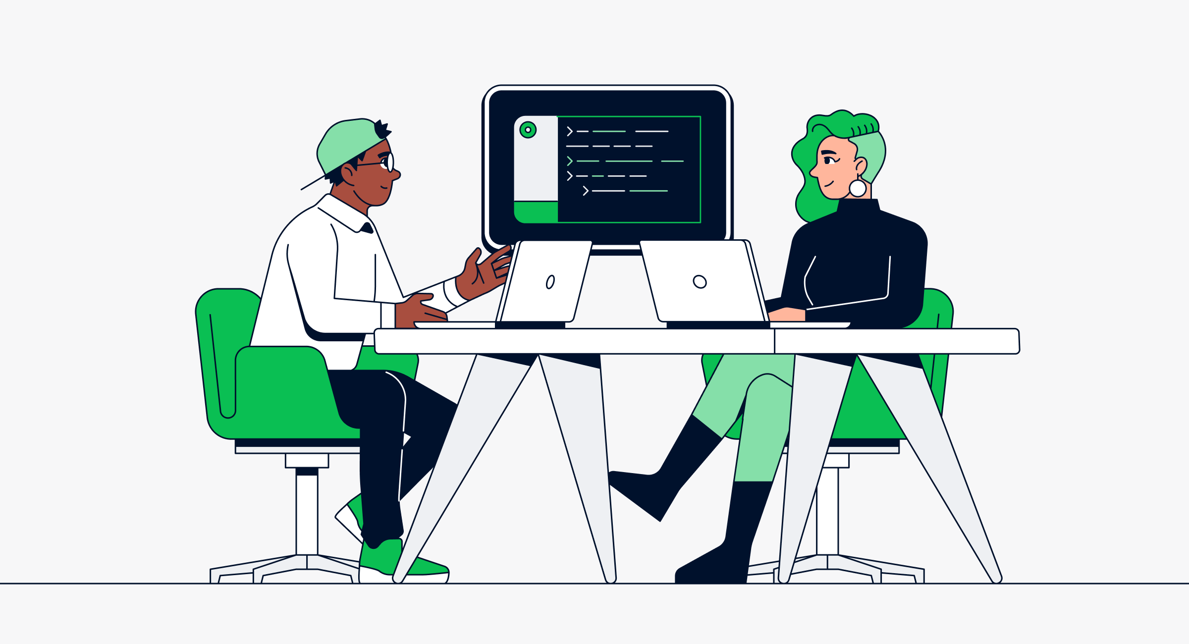 Two people working at a desk with computers and a monitor displaying code.