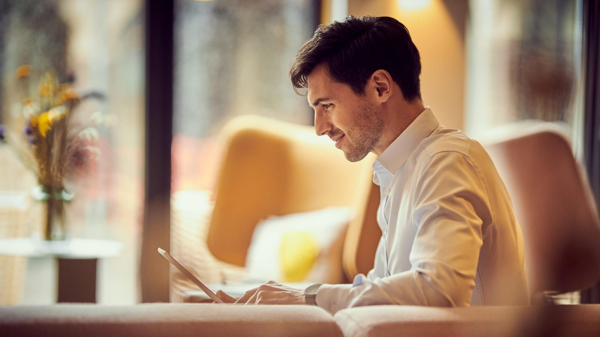 Man sitting and smiling while using a tablet in a well-lit room.