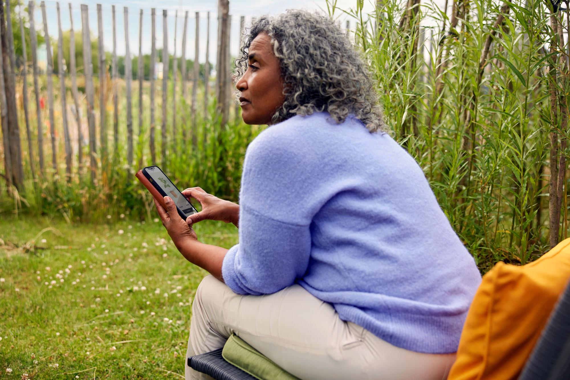 A garden center customer shopping for plants from her phone while sitting in a garden.
