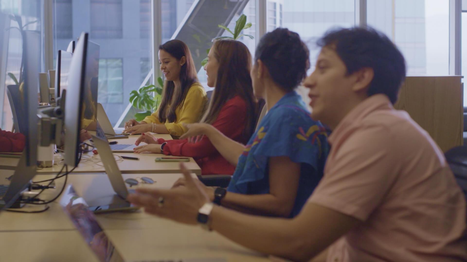 Un grupo de colegas trabajando en computadoras en un entorno de oficina luminoso.