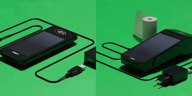 Two Adyen card payment terminals with charging cables and a paper roll on a green background.