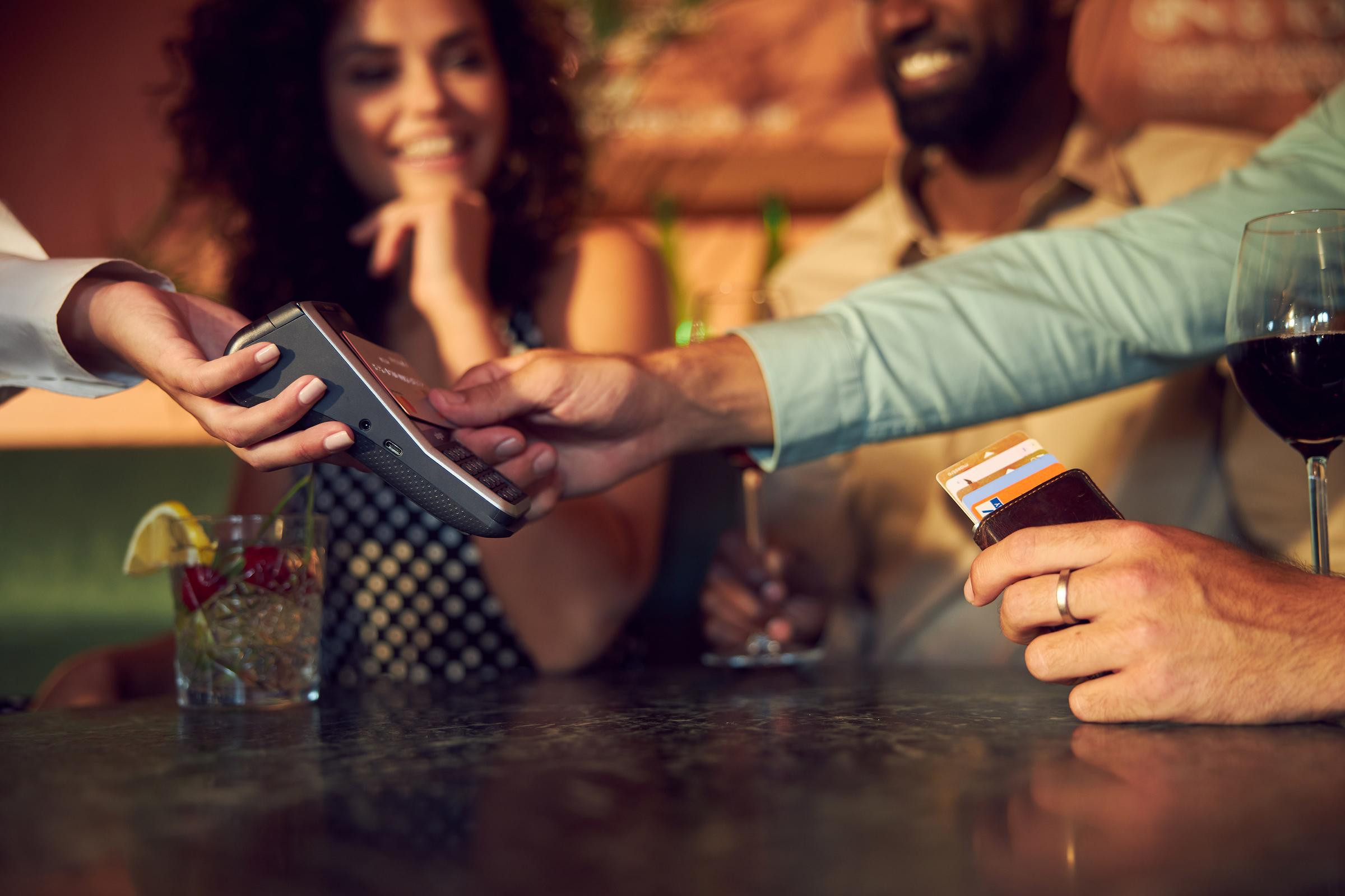 Person using a contactless card with Adyen POS terminal with customers in the background.