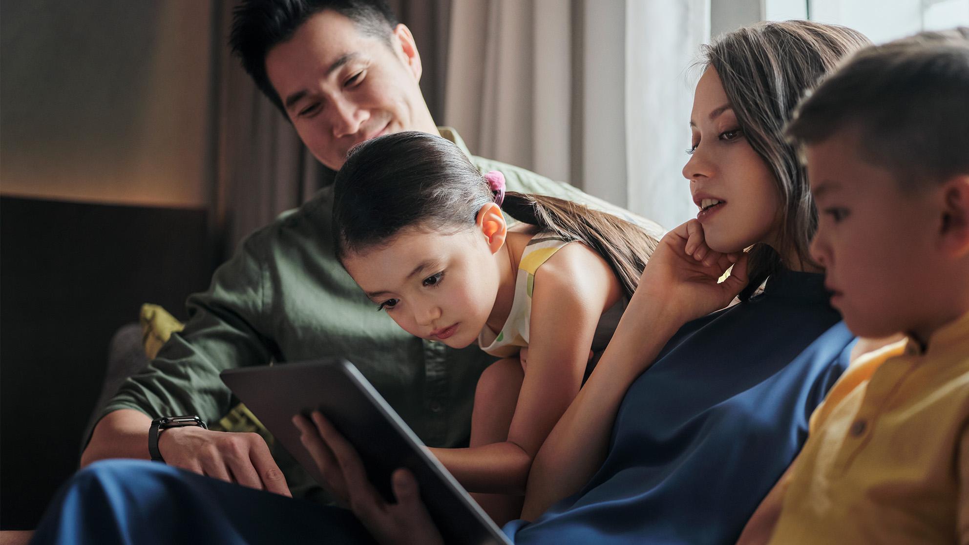 Family of four engaged with a digital tablet while relaxing together indoors.