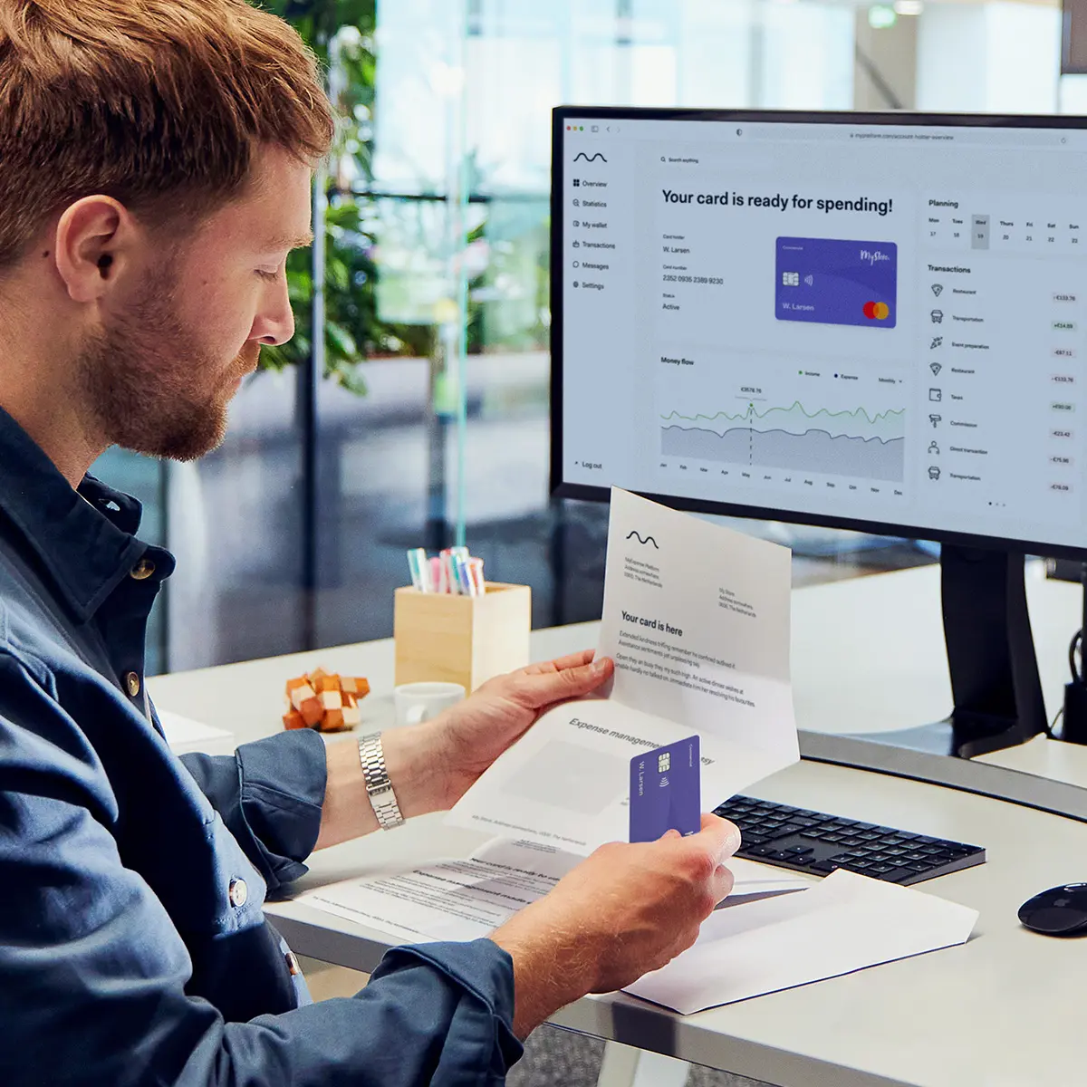 Person at a desk examining a new card next to a computer screen displaying Adyen banking interface.