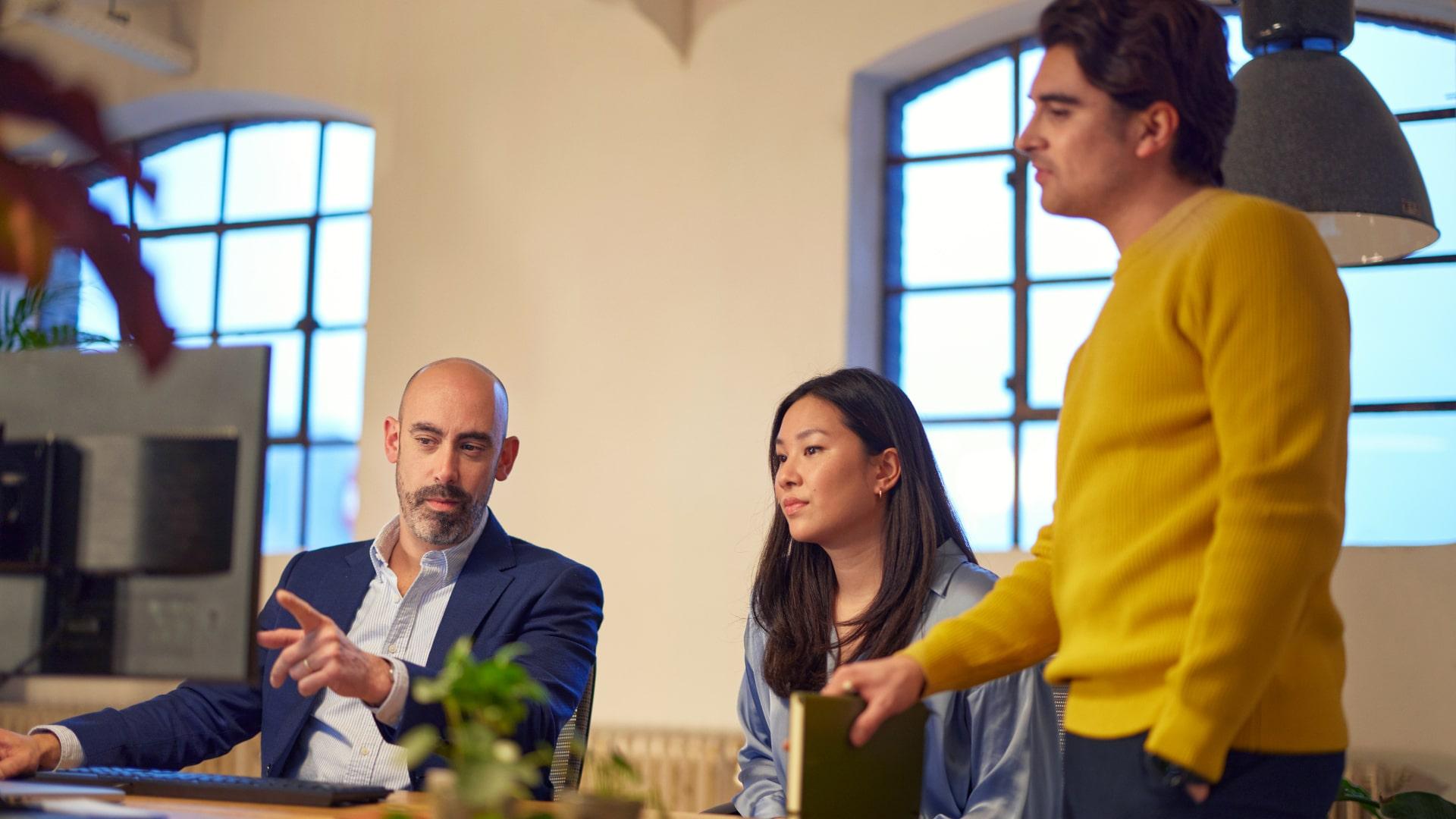 Three professionals engaged in a discussion in a brightly lit office.