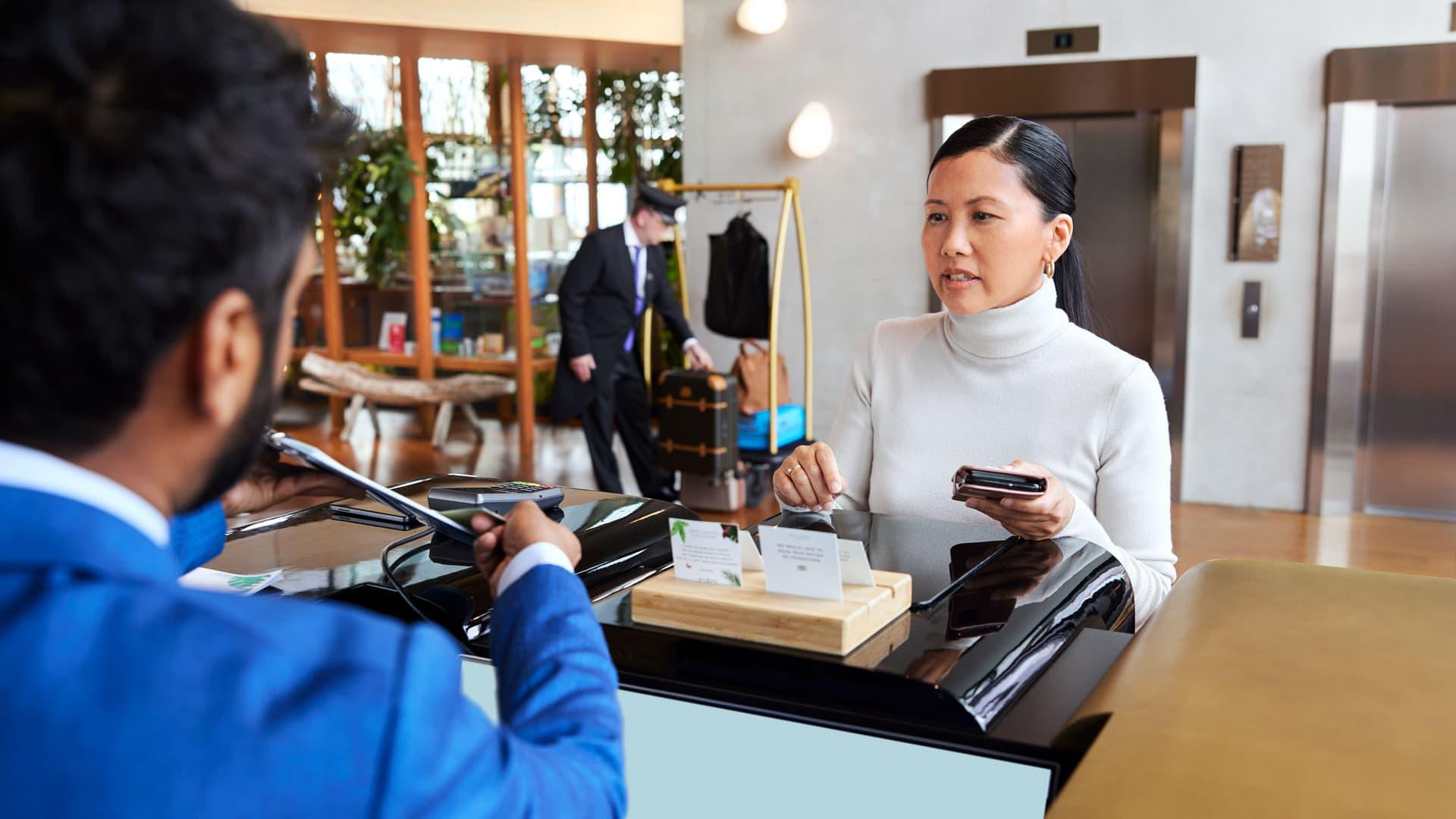 Woman checking out at hotel reception using mobile device for payment.