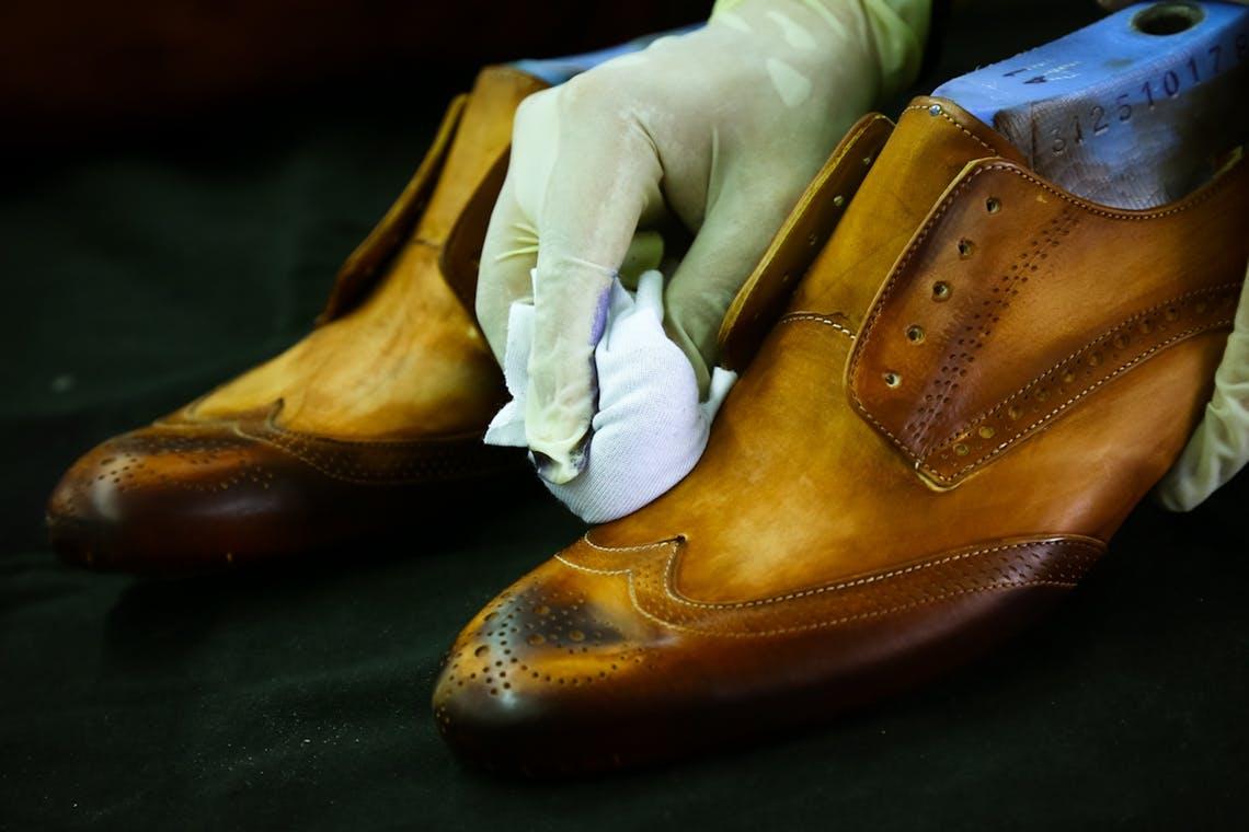 Gros plan d'une personne portant des gants en train de cirer des chaussures en cuir marron.