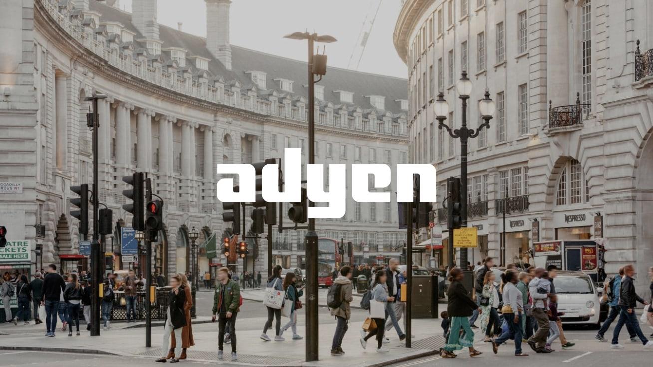 Busy street corner in a city with pedestrians and Adyen logo overlay.