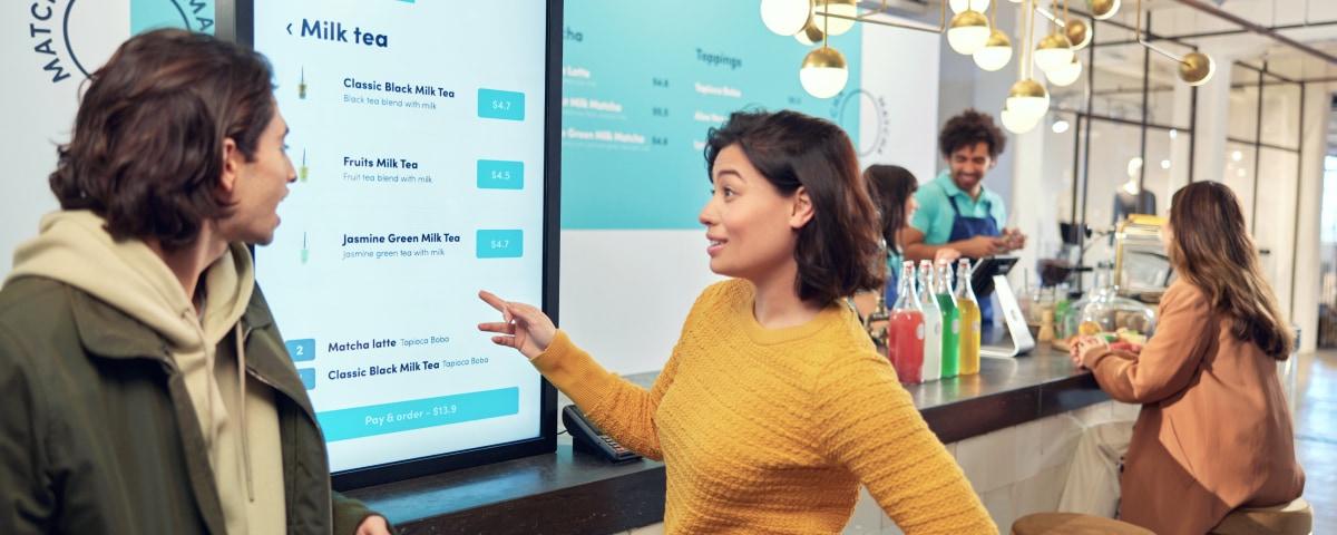 Zákazníci objednávají nápoje v moderní kavárně s digitálním menu displejem s platebním zpracováním Adyen