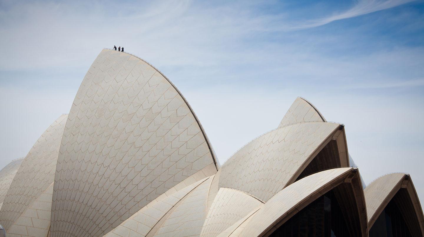 Close-up view of the Sydney Opera House with people on the rooftop.