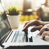 Nahaufnahme von Händen, die auf einer Laptop-Tastatur tippen.