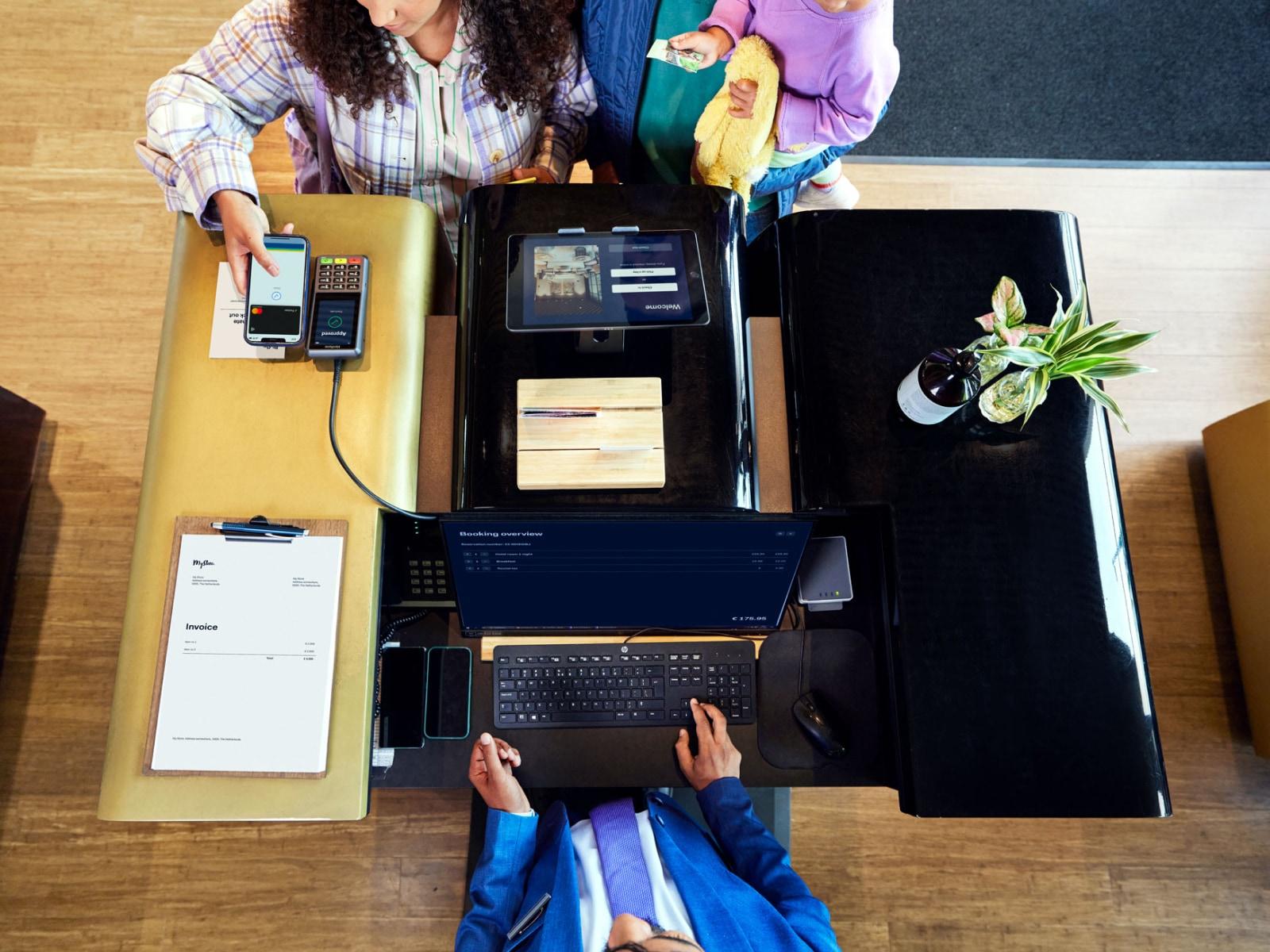 Vista aerea di due persone al bancone cassa con un cliente che utilizza un telefono per il pagamento su un terminale Adyen