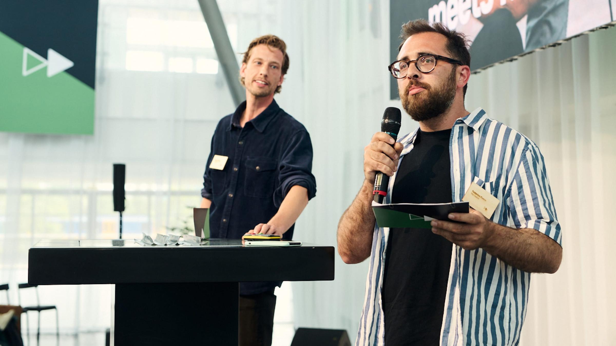 Two men presenting at a conference with one speaking into a microphone.