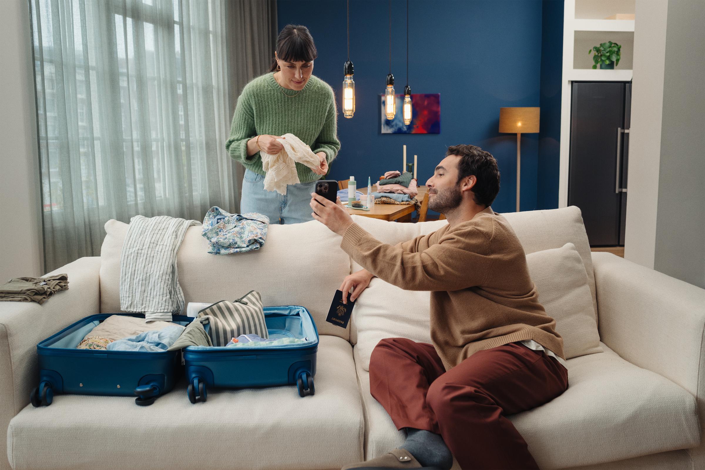 a couple in a living room, packing their suitcase while looking at a phone
