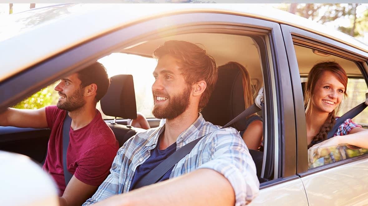 Três amigos desfrutando de uma viagem de carro, com um homem dirigindo e sorrindo.