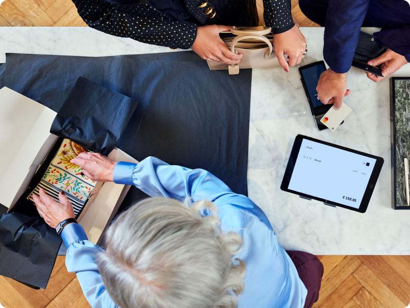 Vista superior de clientes en el punto de pago utilizando el sistema de punto de venta de Adyen con una tableta que muestra el monto de la transacción.