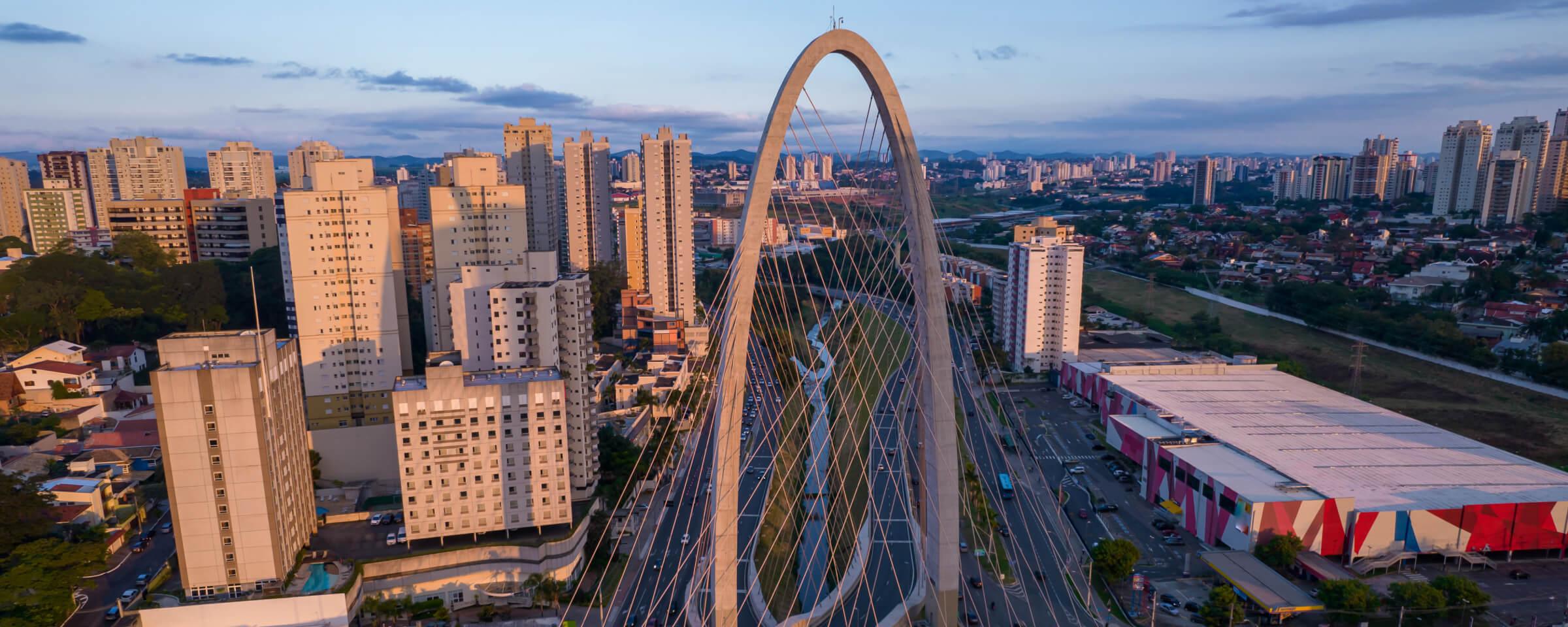 Vista aérea de un puente atirantado moderno sobre una autopista en un área urbana al anochecer.
