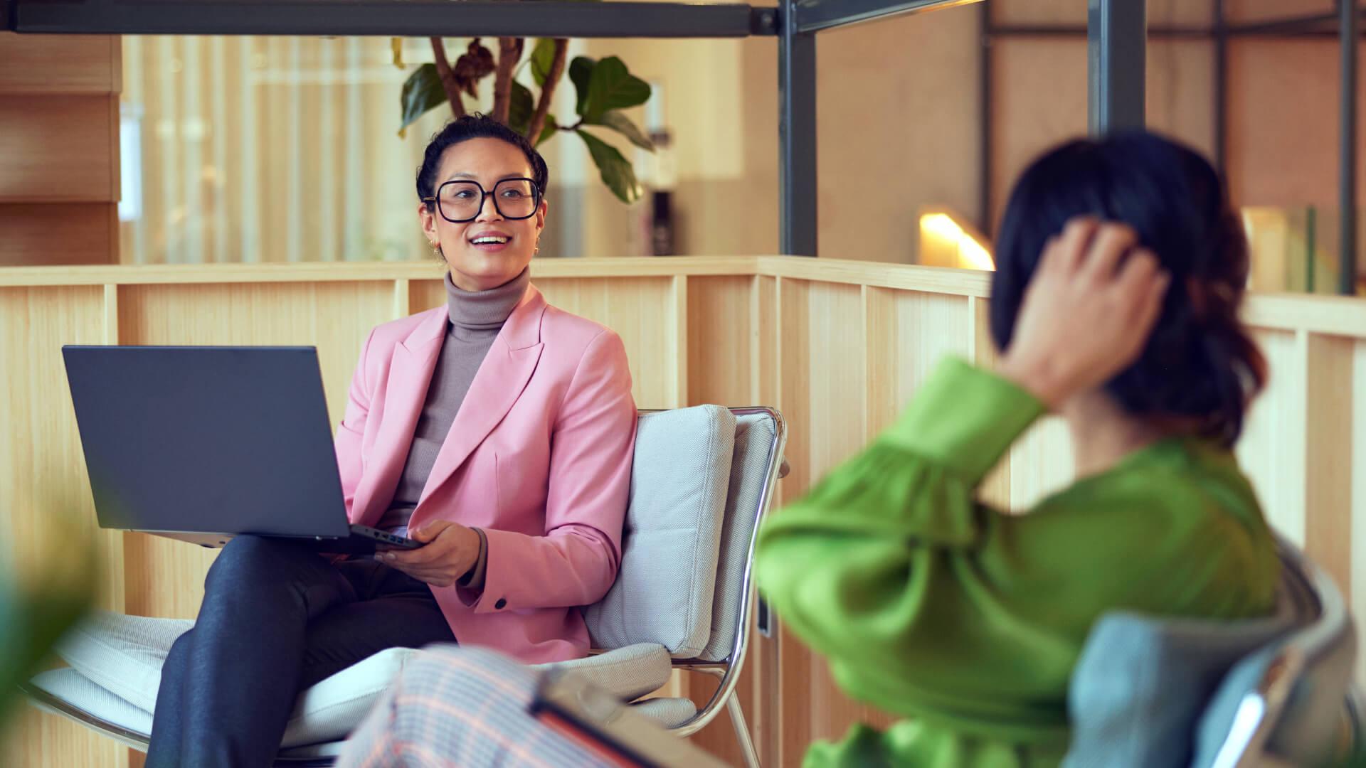 Duas mulheres profissionais em conversa, uma com laptop sorrindo para a outra.